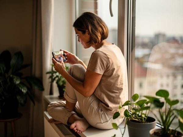 Een vrouw bekijkt familiefoto's op haar telefoon bij het raam